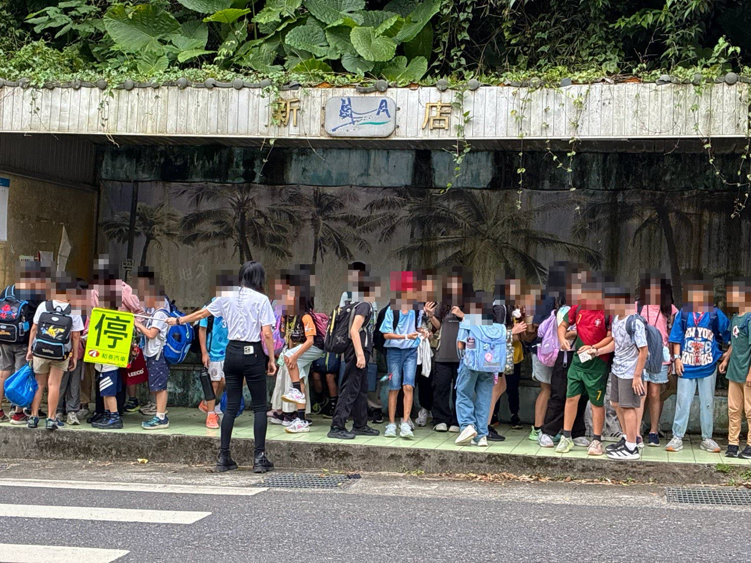 活動照片：孩子們在候車亭排隊等校車，志工在一旁舉牌引導